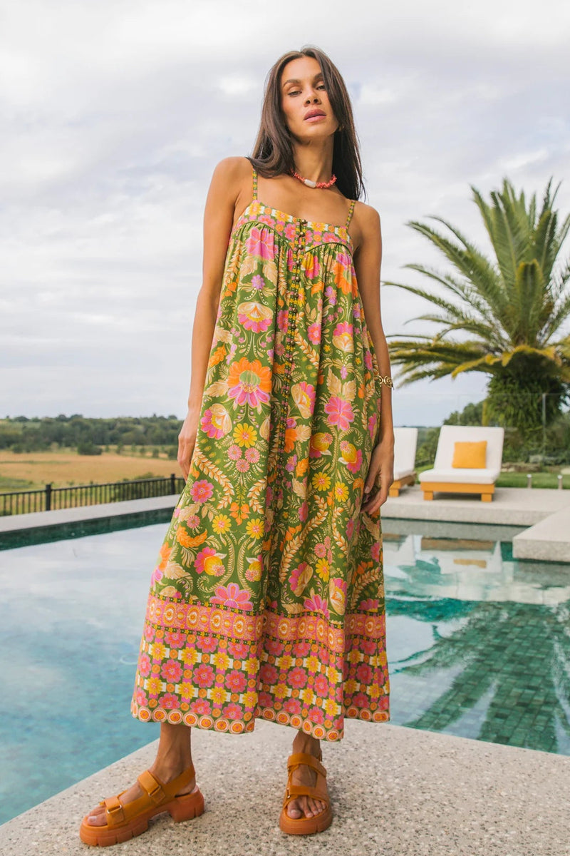 Woman in a colorful floral dress standing by a pool with palm trees in the background
