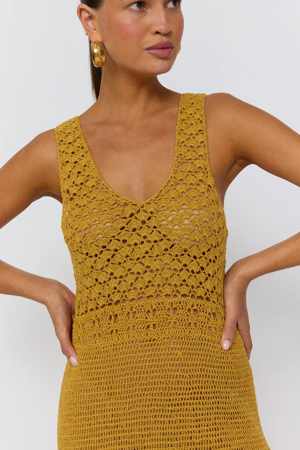 Woman wearing a mustard yellow crochet dress against a plain background