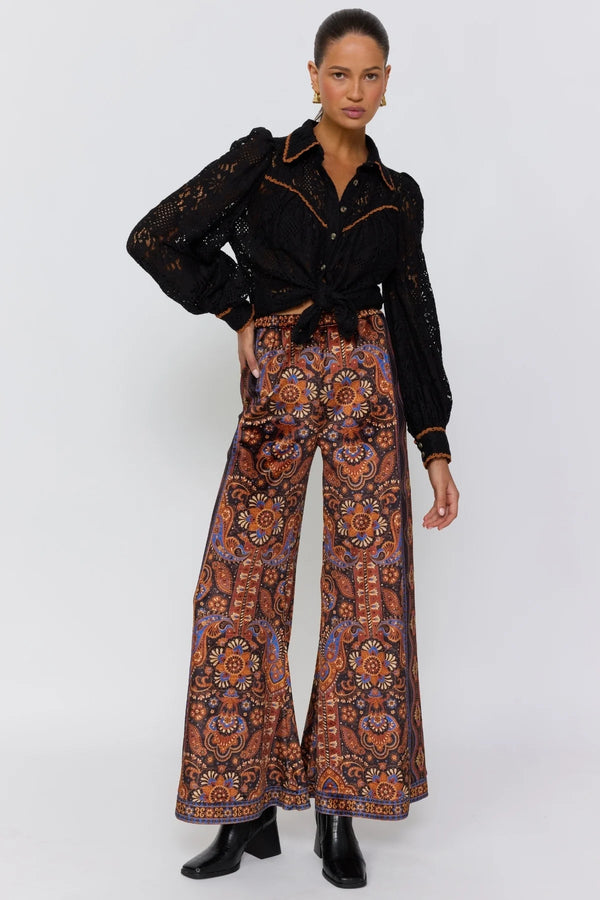 Woman wearing a black embroidered top and patterned pants on a white background