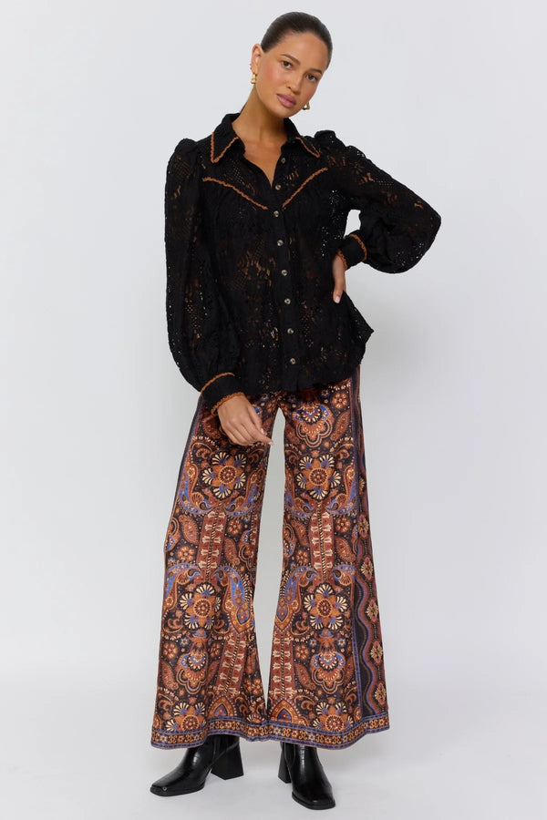Person wearing a black patterned jacket and wide-leg pants on a white background