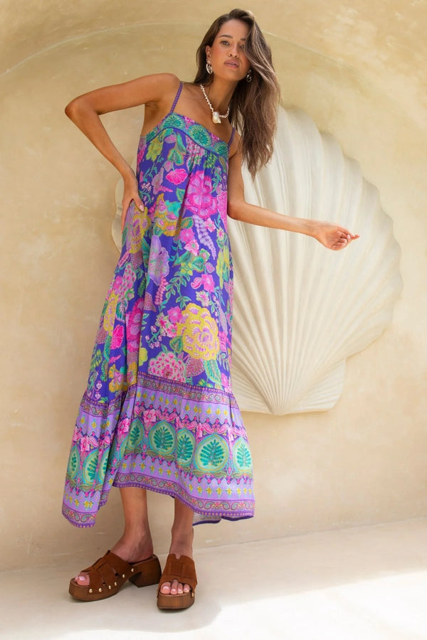 Woman wearing a colorful floral dress standing against a beige wall with a large shell decoration.