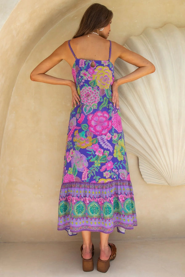 Woman wearing a colorful floral dress standing against a beige wall.