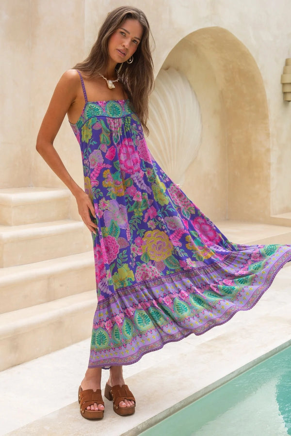 Woman wearing a colorful floral dress standing by a pool with a stone archway in the background.