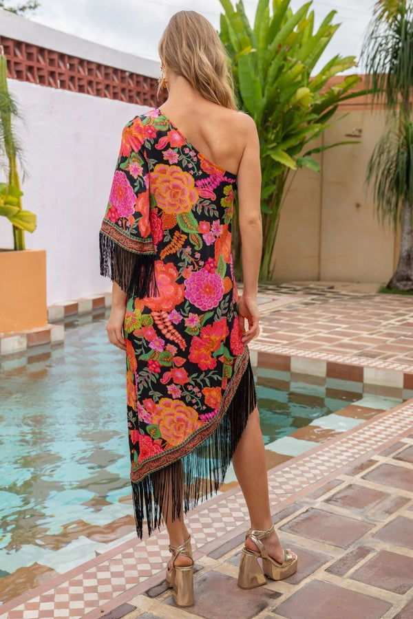 Woman wearing a colorful floral dress with fringe by a poolside.
