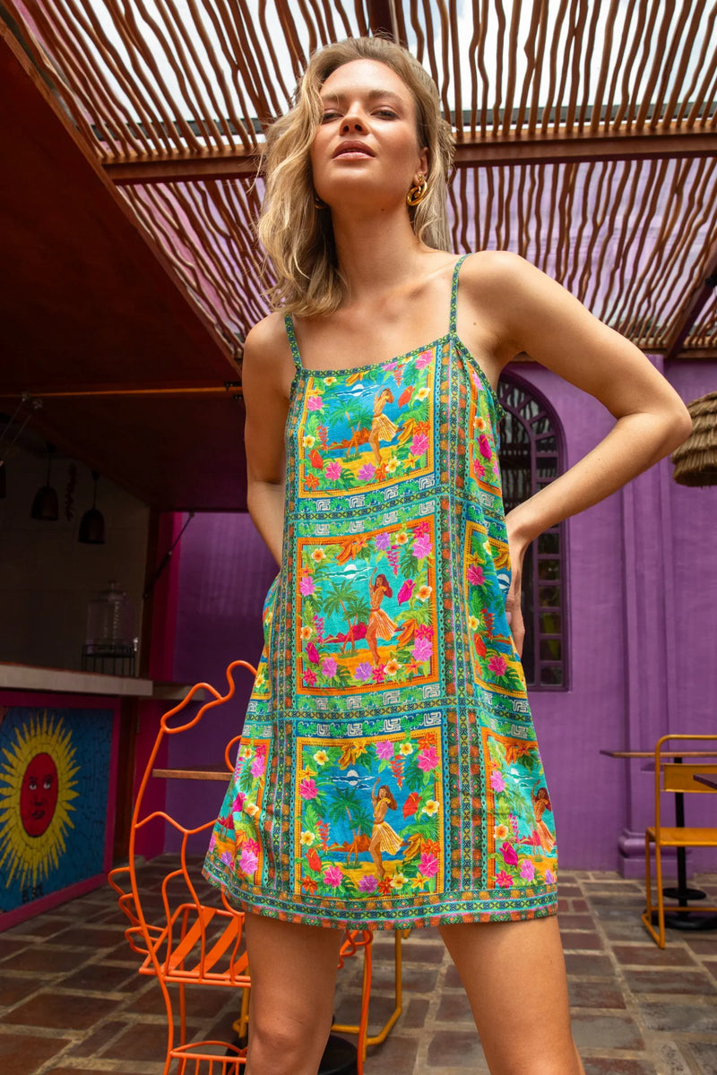 Woman wearing a colorful dress in an outdoor setting with a purple wall and wooden roof.