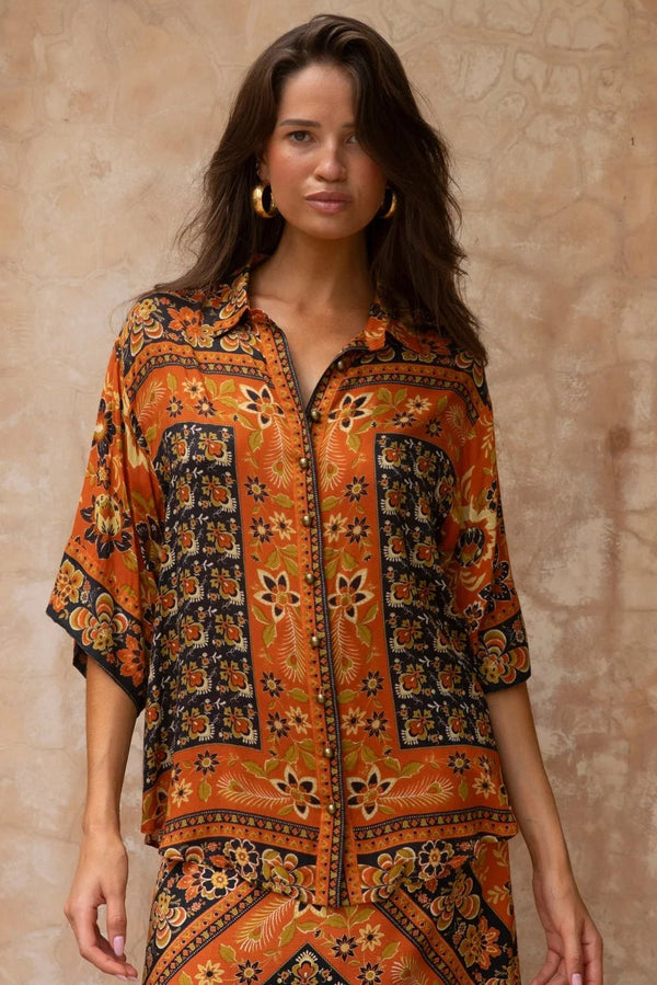 Woman wearing a patterned orange and black outfit against a beige wall.