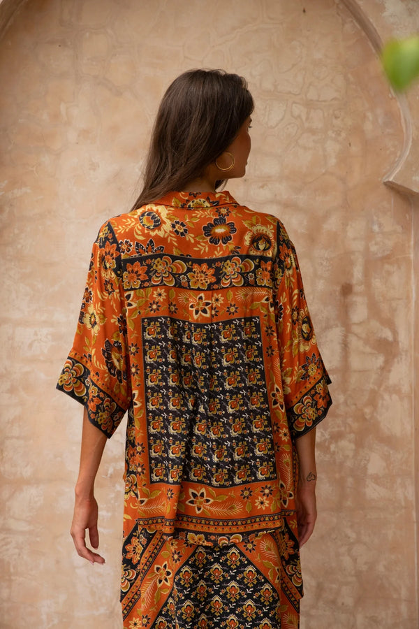 Woman wearing a patterned orange and black dress against a beige wall.