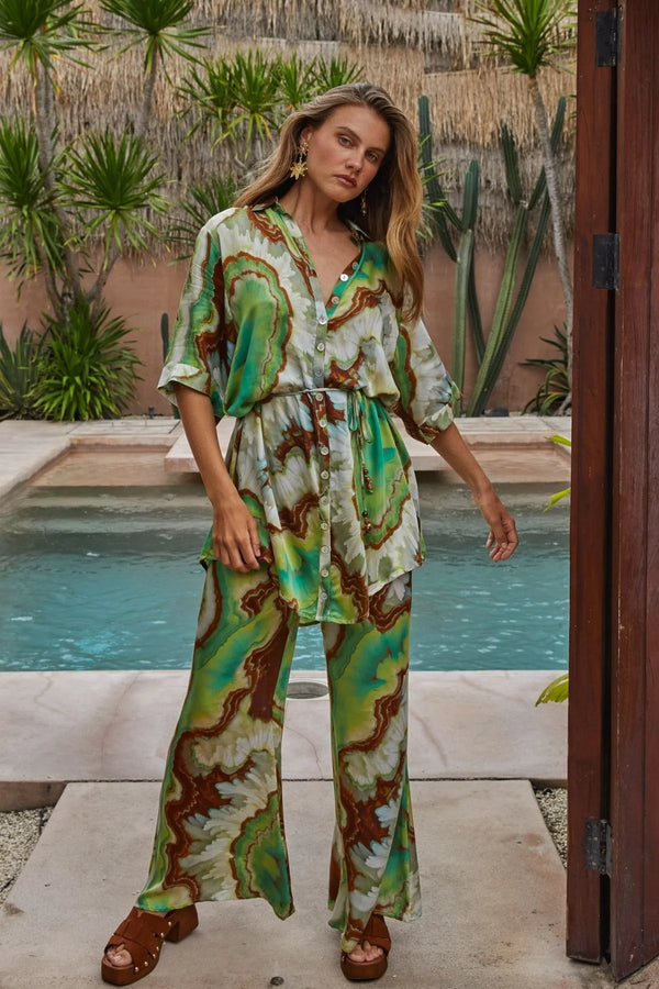 Woman in a patterned outfit standing by a pool with a garden background