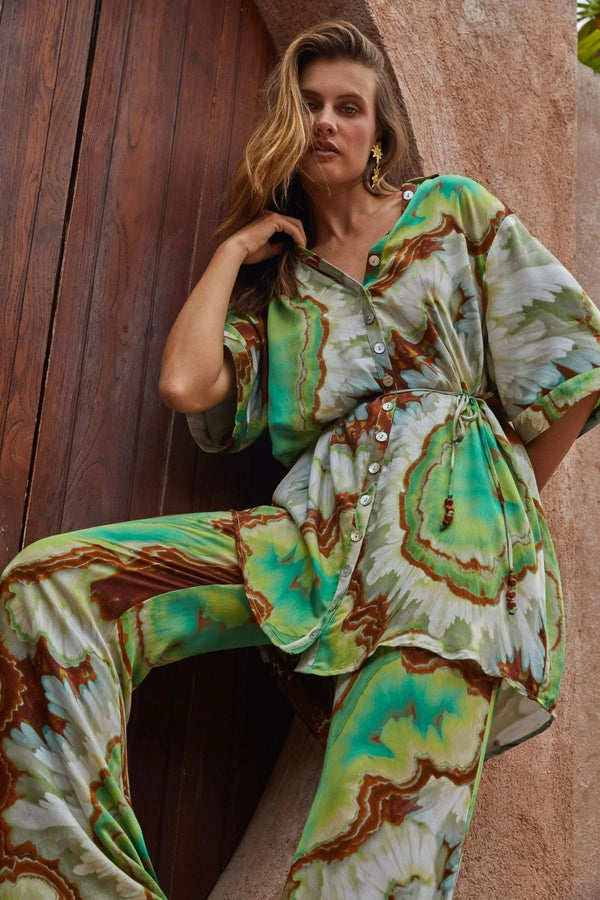 Woman wearing a patterned outfit standing against a textured wall.
