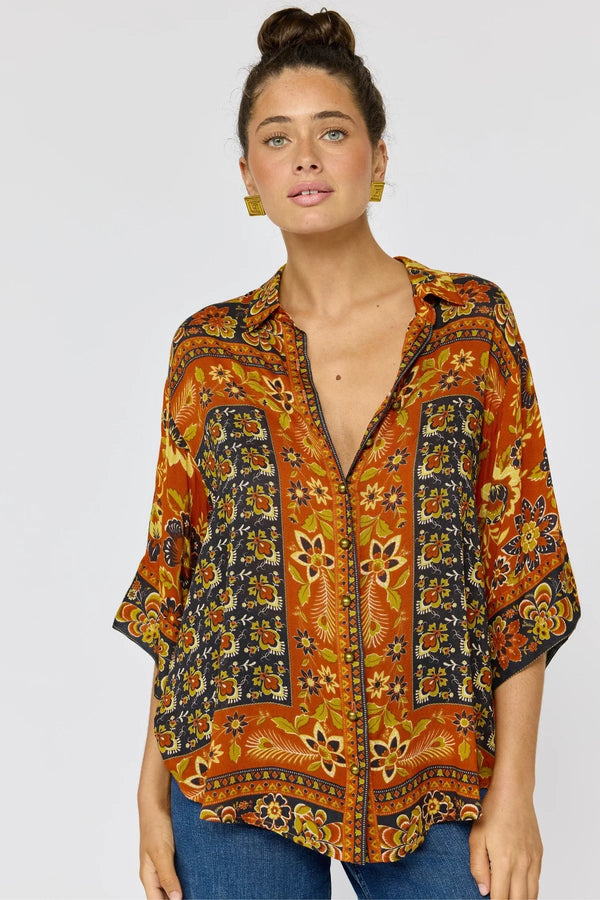 Woman wearing a patterned orange and black blouse against a plain background