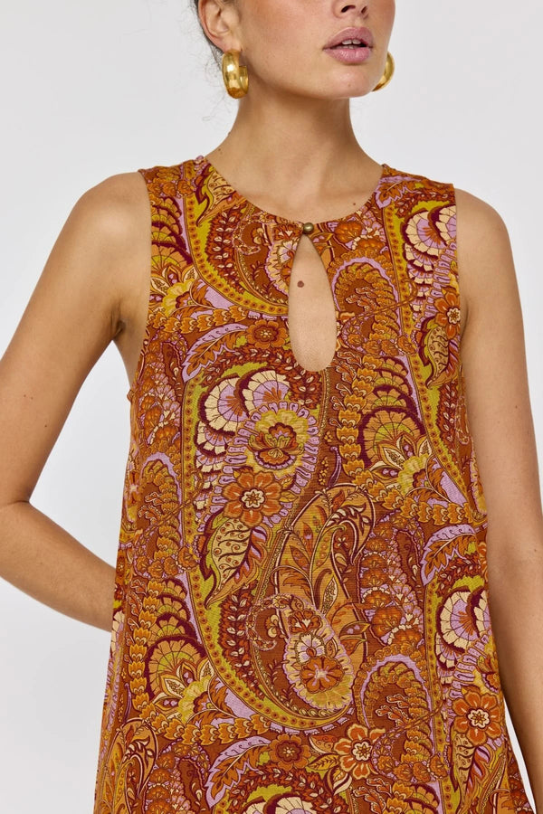 Woman wearing a sleeveless dress with a paisley pattern on a plain background
