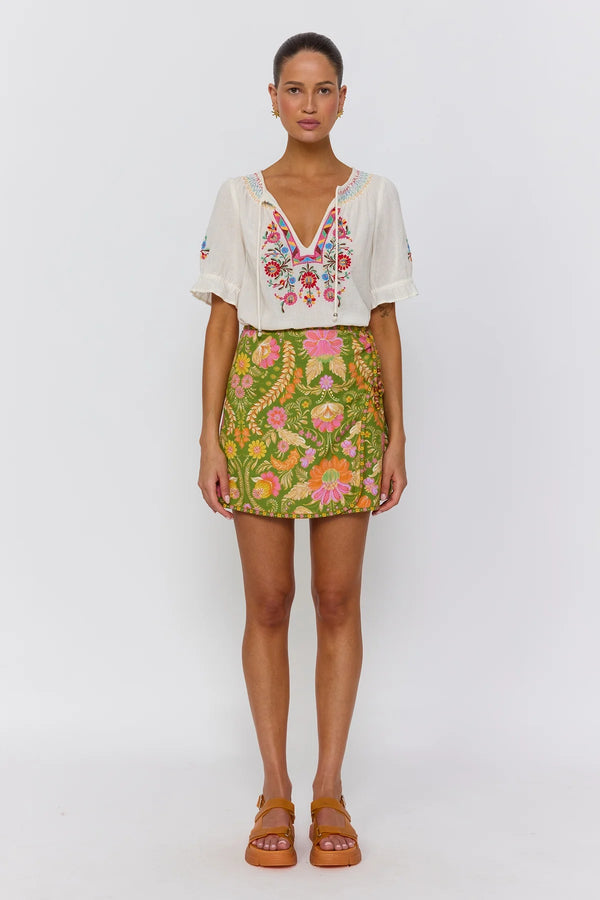 Woman wearing a white embroidered top and a colorful floral skirt on a white background