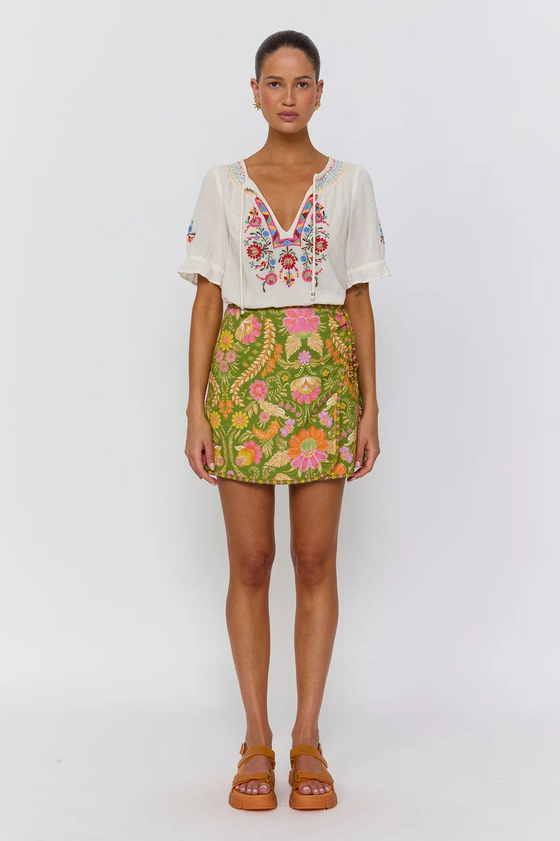 Woman wearing a white embroidered top and a colorful floral skirt on a white background