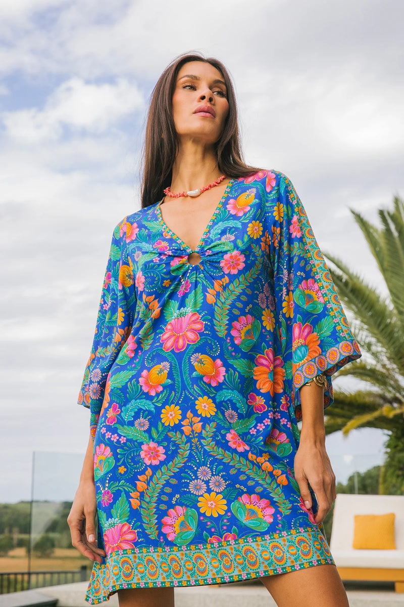 Woman wearing a colorful floral dress with a palm tree and cloudy sky in the background