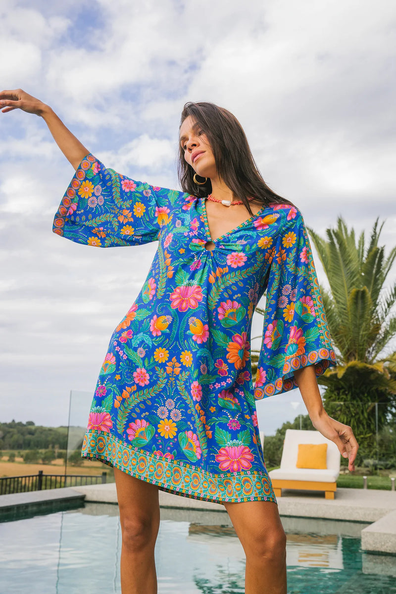 Woman wearing a colorful floral dress by a pool with palm trees in the background