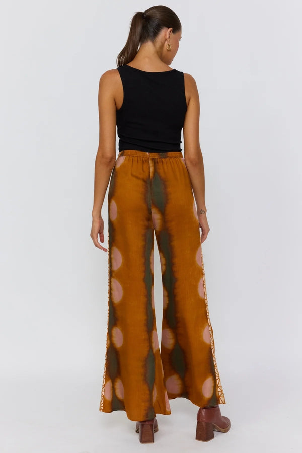 Person wearing a black sleeveless top and brown polka dot pants on a white background