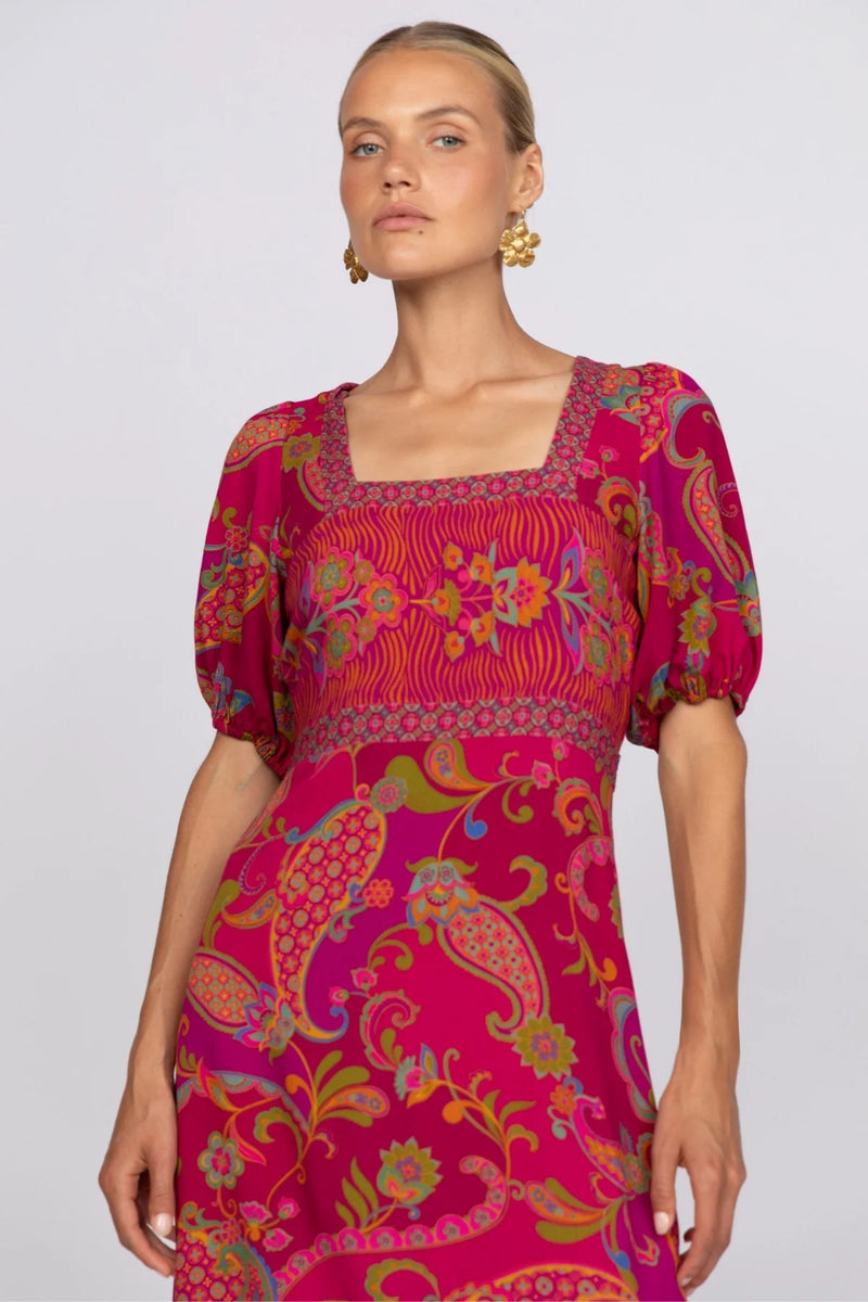 Woman wearing a vibrant pink dress with colorful patterns on a white background