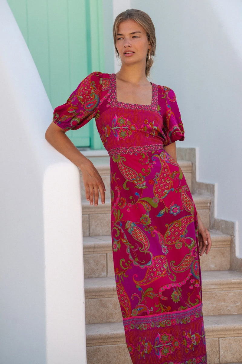 Woman wearing a vibrant pink dress with intricate patterns on a staircase.