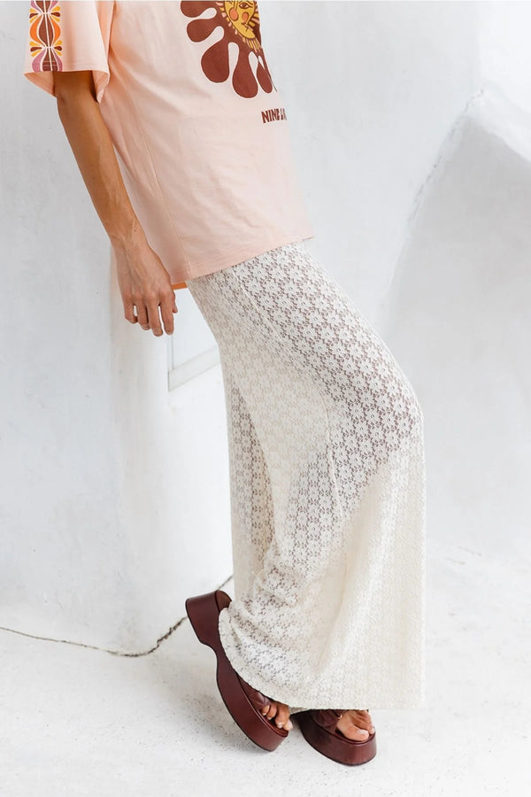 Person wearing a light pink top with floral designs and white lace pants on a white background