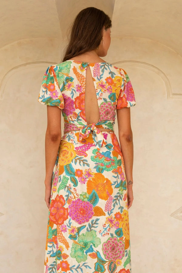 Woman wearing a colorful floral dress with a backless design against a neutral wall.
