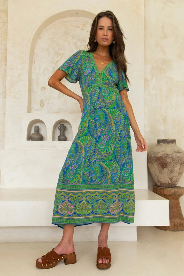 Woman wearing a green patterned dress standing in a decorative indoor setting.