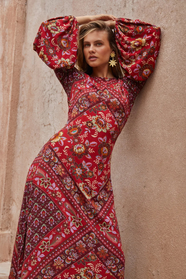 Woman wearing a red floral dress against a beige wall