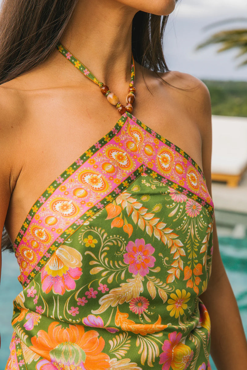 Woman wearing a colorful floral dress with a pool and palm trees in the background