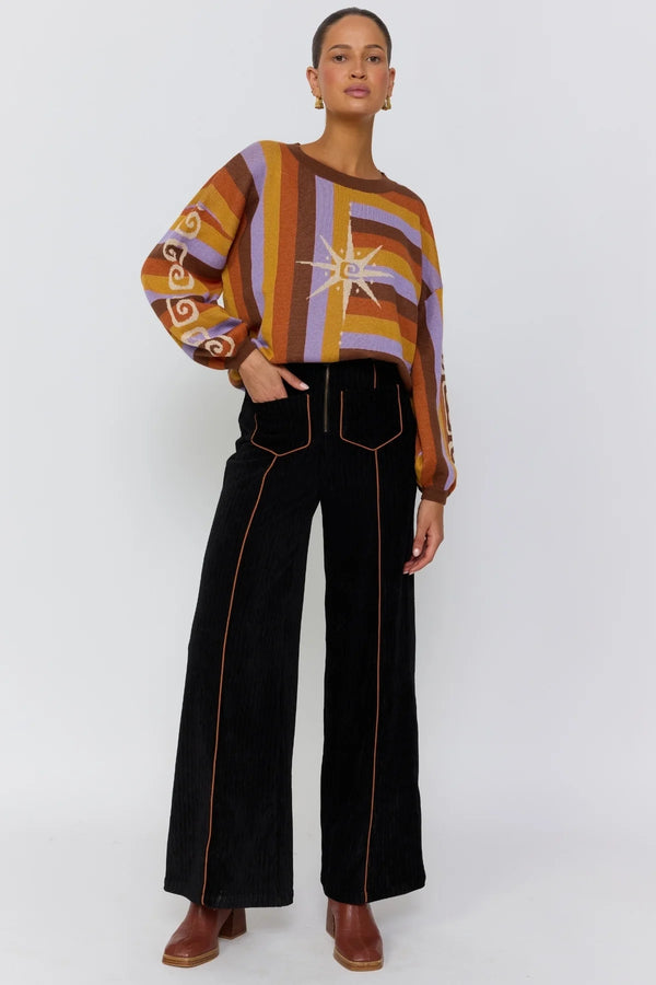 Woman wearing a patterned sweater and black pants on a white background