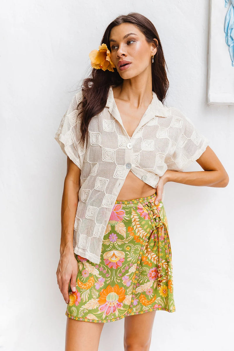 Woman wearing a white blouse and floral skirt against a white wall.