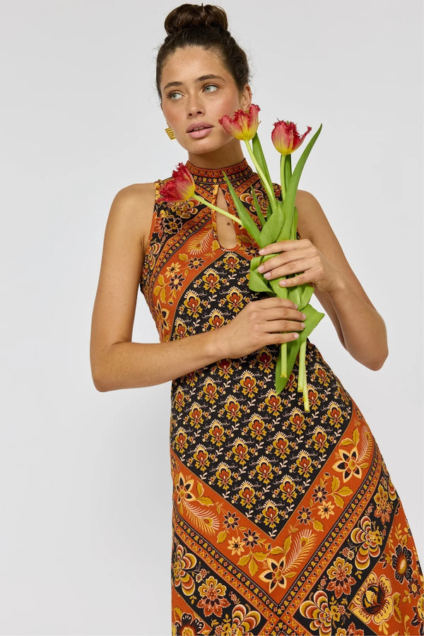 Woman wearing a patterned dress holding tulips against a plain background
