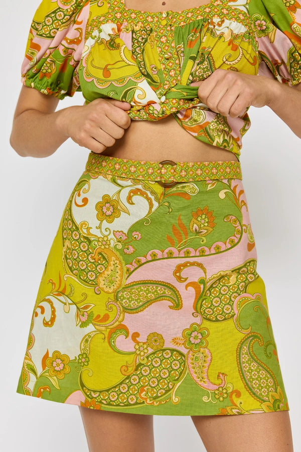 Person wearing a colorful patterned outfit with a green skirt and top on a white background