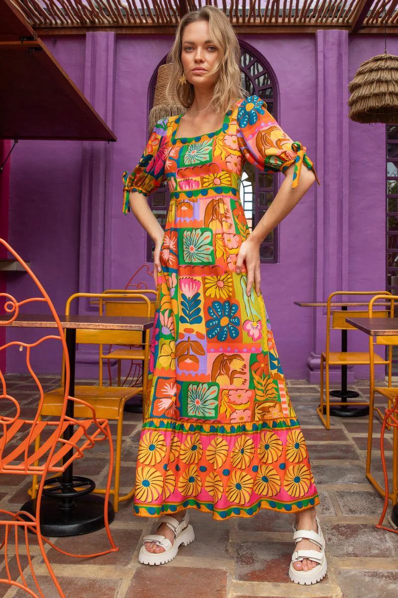 Woman wearing a colorful dress in a vibrant indoor setting with purple walls and orange chairs.