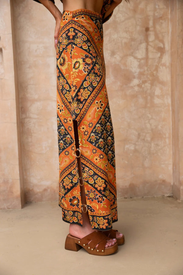 Person wearing a patterned orange and black skirt with a neutral background