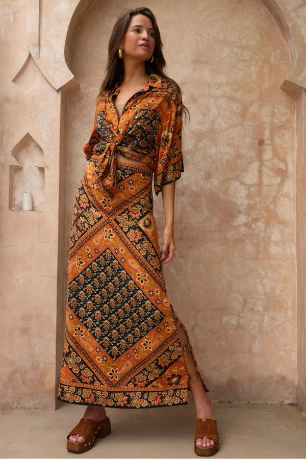 Woman wearing a patterned orange and black dress standing in front of a beige archway.