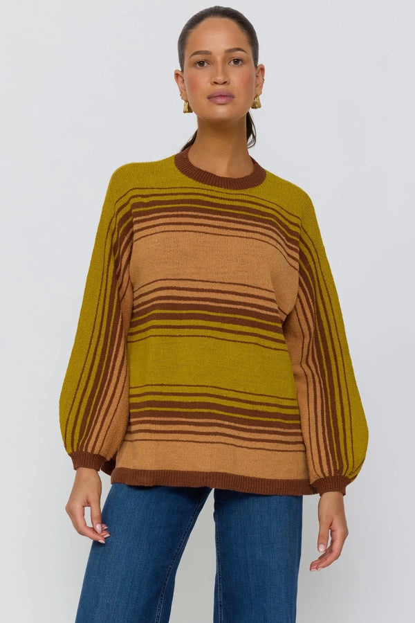 Woman wearing a mustard and brown striped sweater with blue jeans on a white background