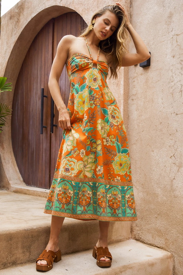 Woman wearing a colorful floral dress standing in front of a stone wall and wooden door.