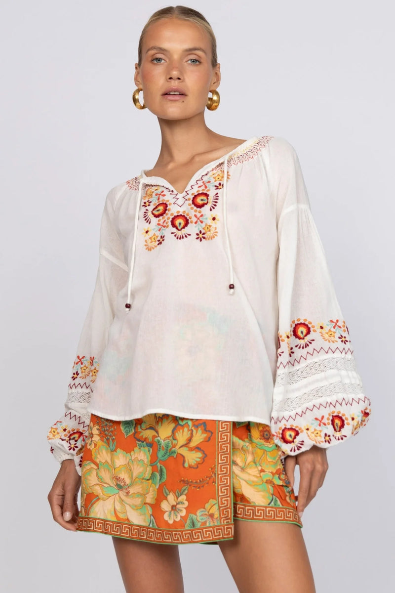 Woman wearing a white blouse with colorful embroidery and a patterned skirt on a plain background