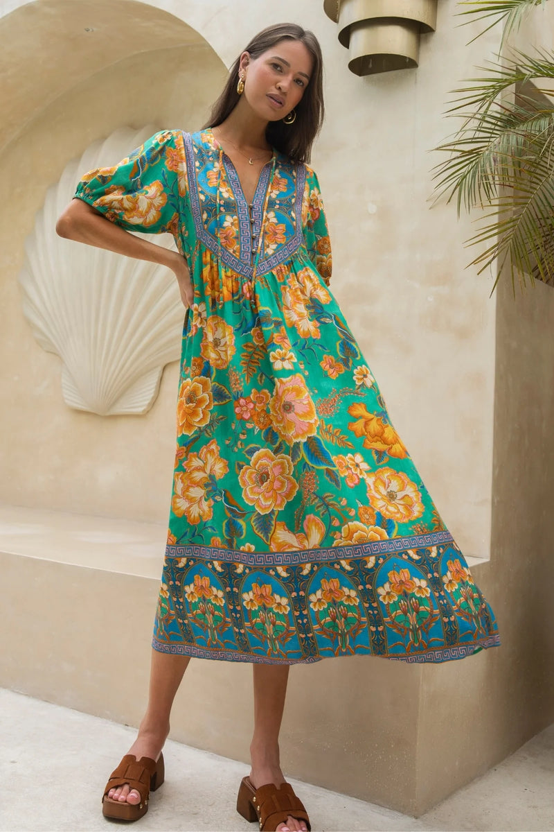 Woman wearing a colorful floral dress standing against a decorative wall.