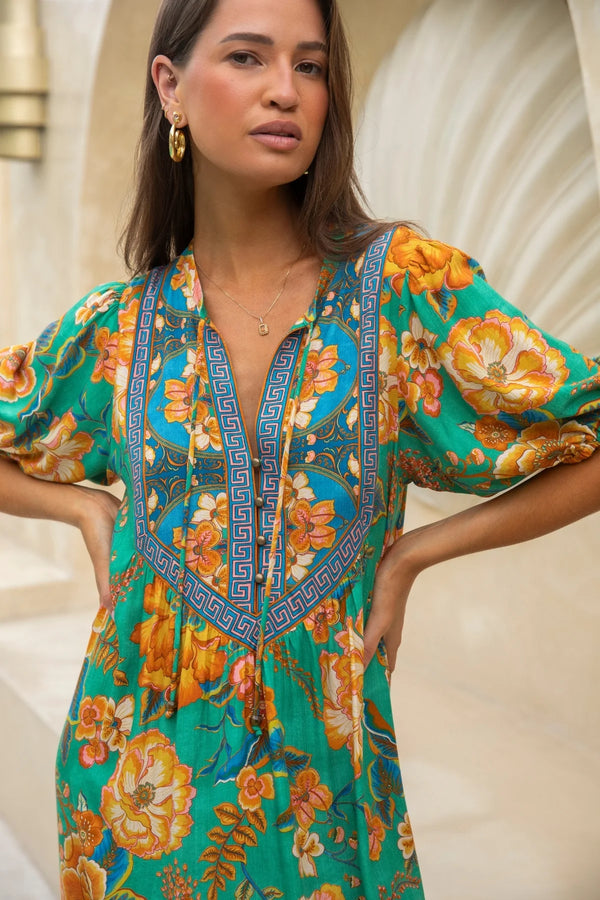 Woman wearing a colorful floral dress with a decorative neckline against a neutral background