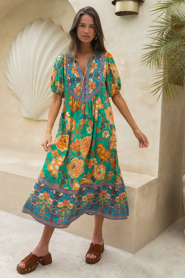 Woman wearing a colorful floral dress standing in a decorative setting with shell art and plants.