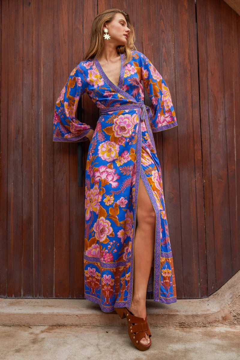 Woman wearing a colorful floral dress against a wooden wall.