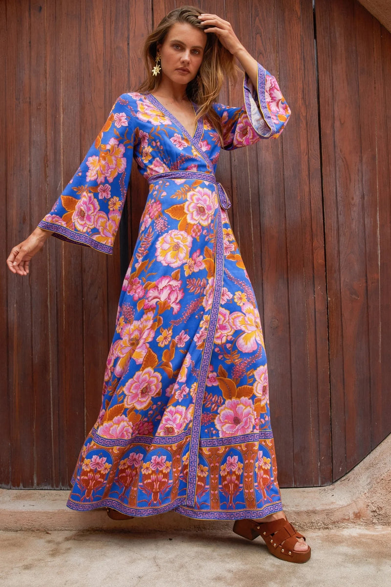 Woman wearing a colorful floral dress against a wooden wall.