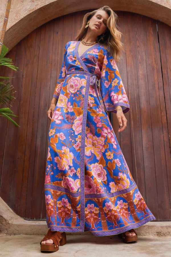 Woman wearing a colorful floral dress standing in front of a wooden door.