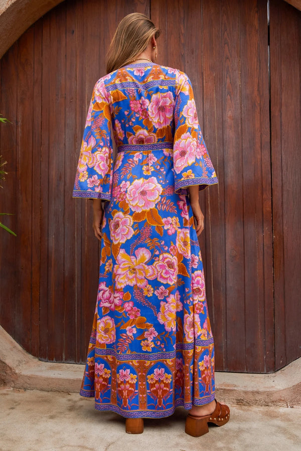 Woman wearing a colorful floral dress standing against a wooden wall.