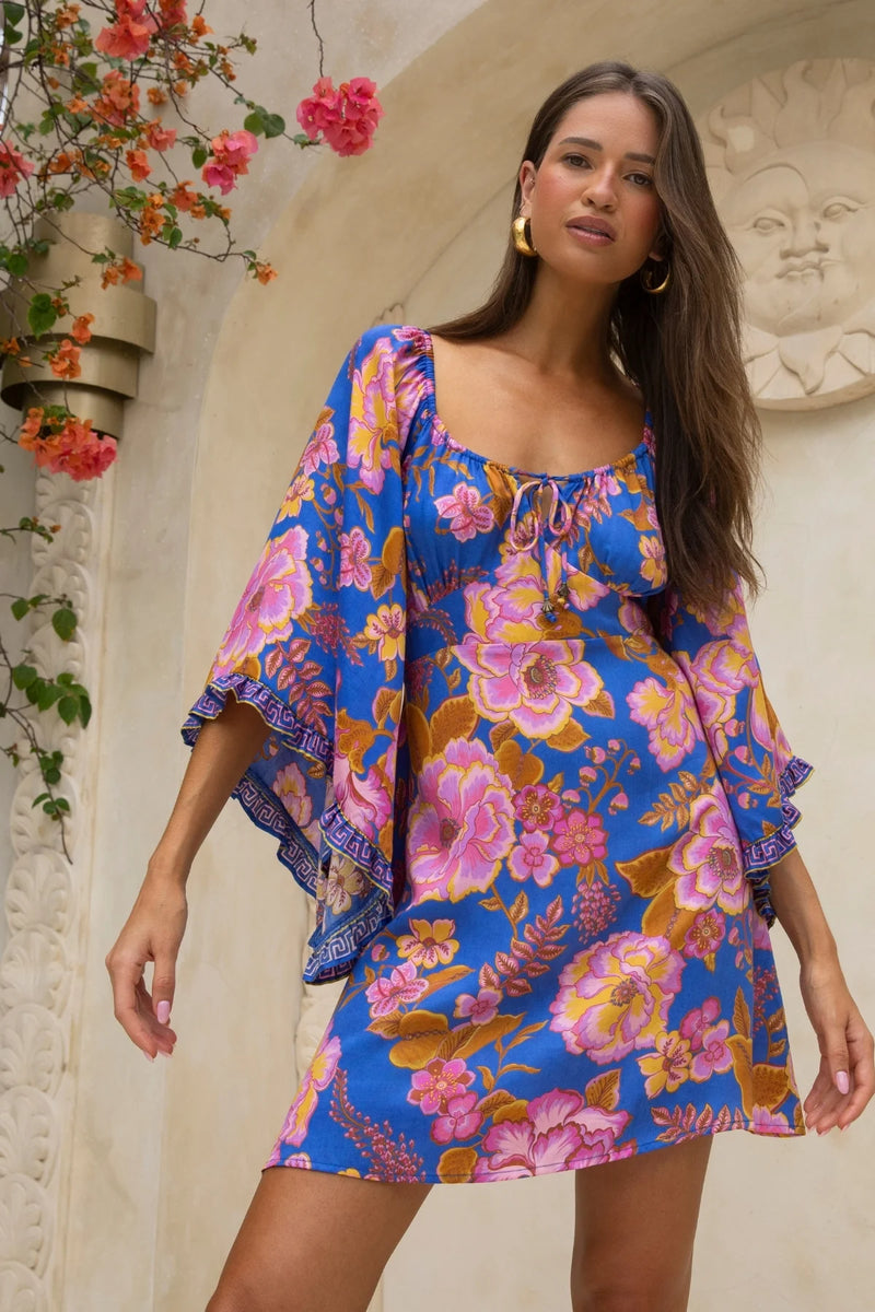 Woman wearing a colorful floral dress standing in front of a decorative wall.