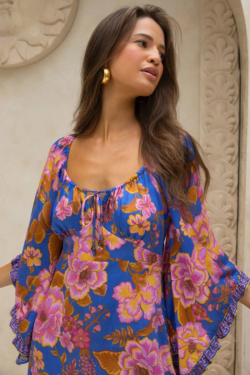 Woman wearing a colorful floral dress against an ornate wall.