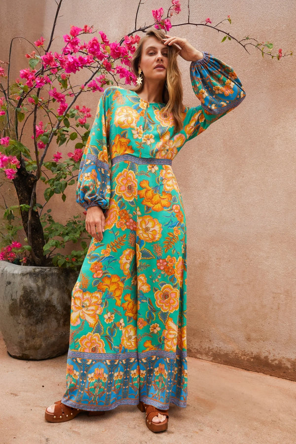 Woman in a floral dress standing next to a potted plant with pink flowers.