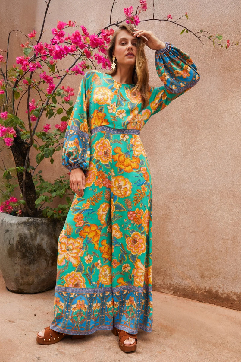 Woman in a floral dress standing next to a potted plant with pink flowers.