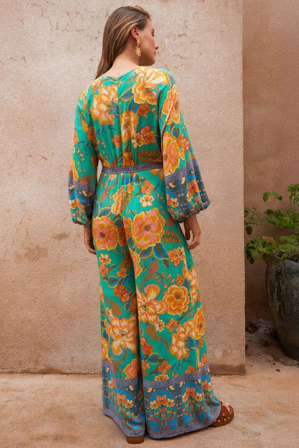 Woman wearing a colorful floral jumpsuit against a beige wall.