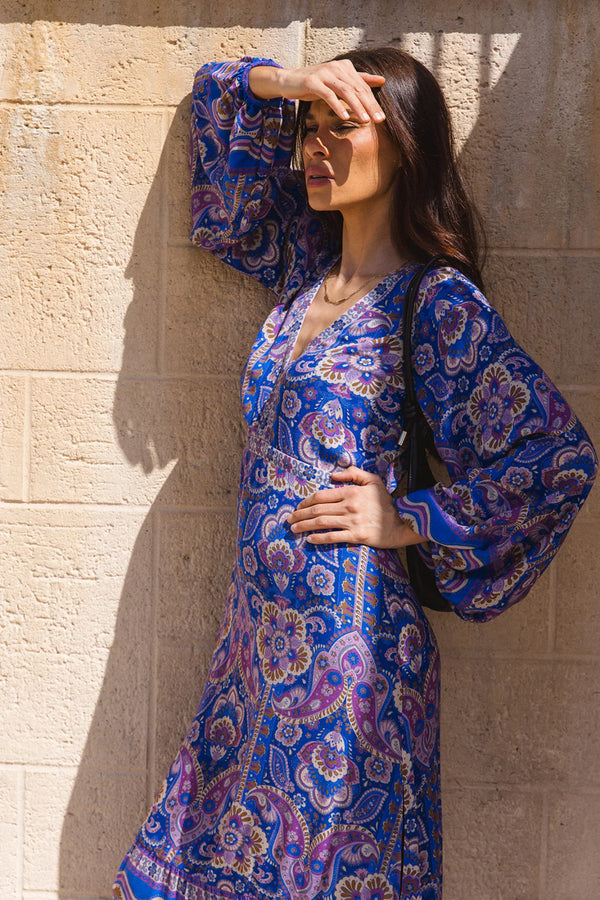 Woman wearing a blue patterned dress against a stone wall.